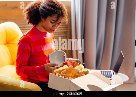 Ein Afrikaner packt eine Pappschachtel im Wohnzimmer des Hauses aus. Ein bezauberndes schwarzes Mädchen ist empört über einen gebrochenen Teller. Eine attraktive junge Frau in Stockfoto