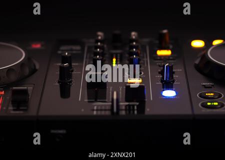 Ein schwarzer DJ-Mixer mit verschiedenen Tasten und Knöpfen, beleuchtet vor dunklem Hintergrund, schafft ein professionelles und rhythmisches Ambiente, Mixer dj-Audio Stockfoto