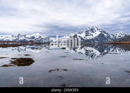 Hohe Berge mit schneebedeckten Gipfeln, die sich bei Flut mit malerischen Wolken im ruhigen Wasser des Fjords spiegeln, Leknes, Lofoten Inseln, Norwegen Stockfoto