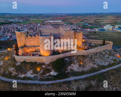 Ein altes Schloss, beleuchtet bei Nacht mit einer Stadt und weiten Feldern im Hintergrund bei Sonnenuntergang, aus der Luft, Consuegra, Toledo, Castilla-La Mancha, Spanien Stockfoto