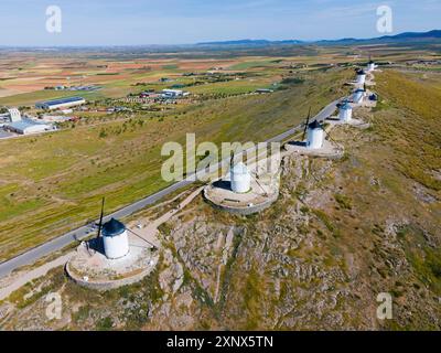 Reihe von Windmühlen auf einem grasbewachsenen Hügel entlang einer Straße mit Blick auf weite Felder und ein Dorf in der Ferne, aus der Luft, Consuegra, Toledo, Castilla-La Stockfoto