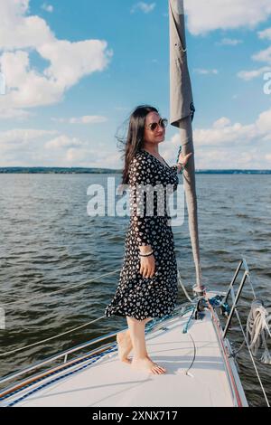 Eine Frau in gemustertem Kleid und Sonnenbrille, die auf einem Segelboot unter klarem Himmel steht. Weißrussland, Minsk Stockfoto