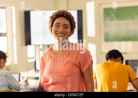 Lächelnder Lehrer im Klassenzimmer mit Schülern, die in der High School an Laptops arbeiten Stockfoto