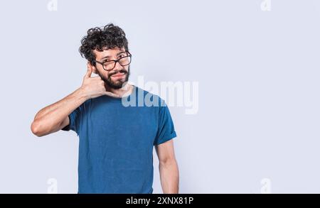 Attraktiver junger Mann imitiert Telefongespräche isoliert. Junger Mann mit Brille, der die Geste des Anrufs isoliert Stockfoto