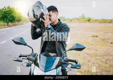 Männlicher Biker auf Motorrad, der einen Sicherheitshelm aufsetzt. Motorradsicherheitskonzept für Biker, junger Motorradfahrer, der draußen einen Sicherheitshelm aufsetzt Stockfoto