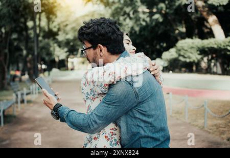 Ein untreuer Mann, der seine Freundin umarmt und auf das Handy schaut. Konzept des untreuen Menschen mit dem Handy. Ein untreuer Mann, der auf die Zelle schaut Stockfoto