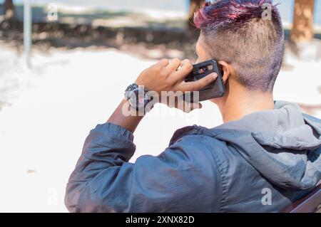 Nahaufnahme eines Mannes, der auf einer Bank sitzt und am Telefon anruft, Nahaufnahme eines jungen Mannes Nahaufnahme eines jungen Mannes, der am Telefon anruft und auf einer Bank sitzt Stockfoto