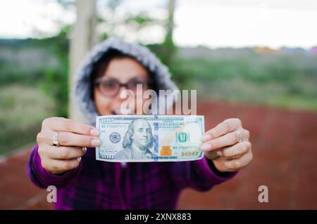 Eine verblüffte Frau, die draußen 100-Dollar-Scheine zeigt Stockfoto