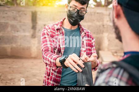 Zwei junge Menschen geben sich gegenseitig eine Maske, Ansicht eines jungen Mannes, der einer anderen Person eine chirurgische Maske gibt, Vorstellung von einer Person, die eine chirurgische Maske gibt Stockfoto