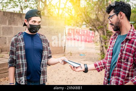 Seitenansicht eines jungen Mannes, der einer anderen Person eine chirurgische Maske gibt, Konzept einer Person, die eine chirurgische Maske gibt, zwei junge Menschen, die einander eine geben Stockfoto