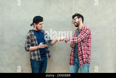 Zwei Teenager-Freunde grüßen sich gegenseitig durch Faustschlag im Freien. Zwei lächelnde junge Jungs, die an einer Wand mit den Fäusten stoßen. Konzept von zwei lächelnden Freunden Stockfoto