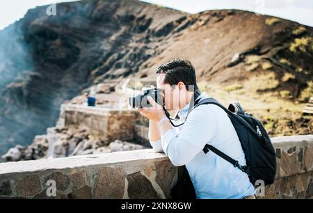 Nahaufnahme eines Touristen, der Fotos an einem vulkanischen Aussichtspunkt macht. Ein Tourist mit einer Fotokamera, der Fotos an einem Aussichtspunkt macht. Abenteuerlustiger Mann mit Stockfoto