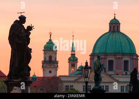 Statue an der Karlsbrücke mit einer Kuppel des hl. Franz von Assisi im Hintergrund bei Sonnenaufgang, UNESCO-Weltkulturerbe, Prag, Tschechische Republik Tschechien Stockfoto