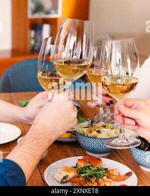 Gruppe von Ernte anonymen Freunden klirren Gläser mit Wein während der Versammlung um Tisch mit köstlichen Gerichten während des Hausdinner Stockfoto