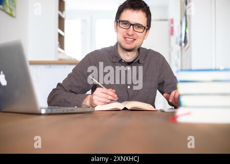 Männliche glückliche Schüler forschen und lernen zu Hause, Stapel von Büchern verschwommen Stockfoto