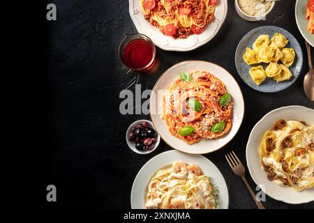 Italienisches Essen, über dem Kopf flacher Lay-Shot. Nudeln, Oliven, Wein auf schwarzem Hintergrund mit Kopierraum. Spaghetti mit Tomatensauce, Ravioli und anderen Stockfoto