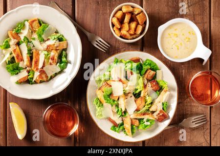 Caesar-Salat, darüber liegende flache Lay Shot mit Croutons, Sauce und Wein auf einem dunklen rustikalen Holzhintergrund Stockfoto