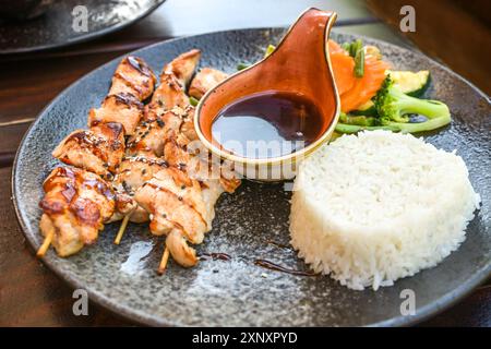 Hähnchenspieße, Jasminreis und Gemüse mit einer scharfen Teriyaki-Sauce, asiatische Gerichte auf einem dunklen Teller, ausgewählter Fokus, enge Tiefe des Fie Stockfoto