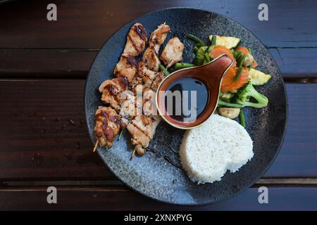 Hähnchenspieße, Jasminreis und Gemüse mit einer scharfen Teriyaki-Sauce, asiatische Gerichte serviert auf einem dunklen Teller und einem Holztisch, Kopierraum, Platte Stockfoto