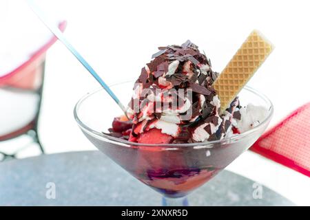 Eisbecher mit Vanille- und Kirschlöffeln, Schlagsahne, rote Fruchtsauce und Schokoladenchips in einem Straßencafé an einem heißen Sommertag in der Stadt, Stockfoto