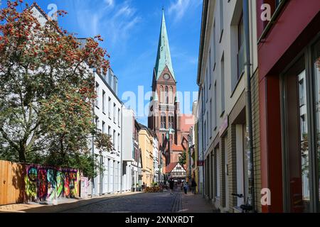 Schwerin, Deutschland, 29. Juli 2024: Enge Fußgängerzone Buschstraße mit kleinen Läden und Straßenrestaurants, die zum St. Marien-Dom in der Stadt führt Stockfoto