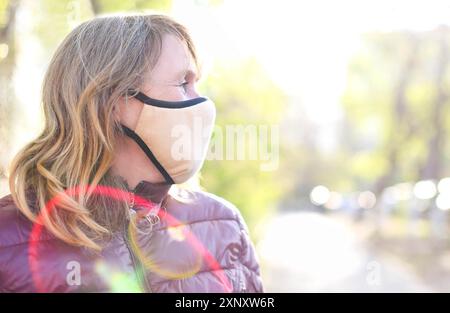 Porträt der mittleren Alter blonde Frau in medizinischen Maske im Freien bei Sonnenuntergang. Corona Virus, Covid-19, Pandemiekonzept Stockfoto