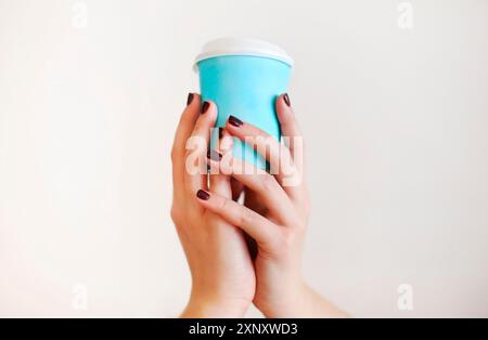 Ernte anonyme Frau in warmen Pullover mit dunkler Maniküre hält Einweg Tasse Kaffee während der Ruhepause am Holztisch Stockfoto