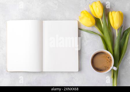 Öffnen Sie leeren Notizblock, gelbe Tulpen und Tasse Kaffee auf grauem Steintisch, in der Draufsicht flacher Lay-Kopierraum Stockfoto