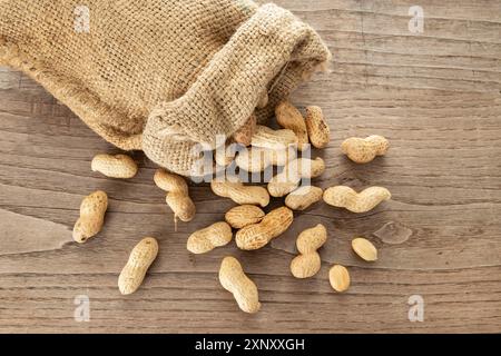 Burlap Sack und Erdnüsse auf rustikalem Holztisch. Arachis hypogäa Stockfoto