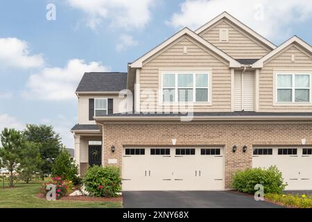 Ein zweistöckiges Vorstadtgebäude mit einer Garage für zwei Autos, braunem Vinyl und Felsenbord und einer wunderschönen Landschaft. Stockfoto