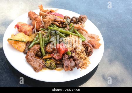 Verschiedene chinesische Fleisch- und Gemüsesorten mit gebratenem Reis auf einem weißen Teller und einem blauen Tisch, Kopierraum, ausgewählter Fokus, enge Schärfentiefe Stockfoto