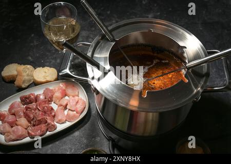 Fondue-Topf mit kochendem heißem Öl, langen Gabeln und rohem Fleisch, Party-Dinner für Freunde und Familie, ausgewählter Fokus, enge Schärfentiefe Stockfoto