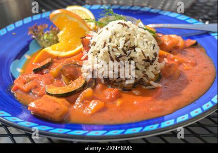 Würzige Tomatensauce mit Gemüse und Fisch serviert mit weißem und schwarzem Reis auf einem blauen Teller, ausgewählter Fokus, enge Schärfentiefe Stockfoto