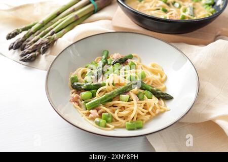 Spaghetti Carbonara Variation mit grünem Spargel serviert auf einem Teller, Zutaten und Serviette auf einem weißen Tisch, Kopierraum, ausgewählter Fokus, schmal Stockfoto