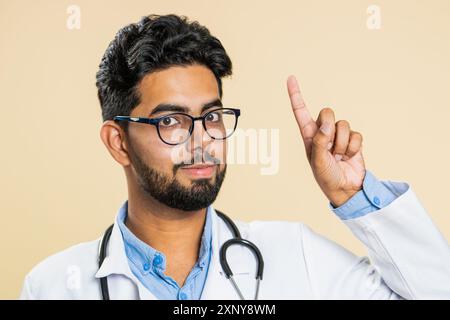 Eureka. Inspirierter junger indischer Arzt Kardiologe Mann, der mit offenem Mund den Finger nach oben zeigt, gute Idee, Plan, Start-up, Inspiration Motivation Lösung hat. Apotheke-Typ auf beigefarbenem Hintergrund Stockfoto