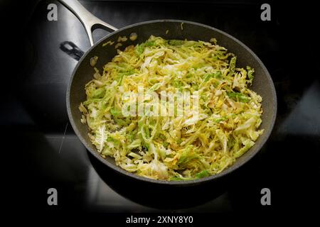 Wirsingkohl in einer Pfanne auf dem schwarzen Herd, zuhause kochen mit gesundem Wintergemüse, ausgewählter Fokus, enge Schärfentiefe Stockfoto