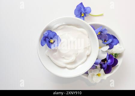 Natürliche kosmetische Salbe und Bratsche oder violette Blüten in weißen Schüsseln auf hellgrauem Hintergrund, Kopierraum, Hochwinkelansicht von oben, ausgewählt Stockfoto