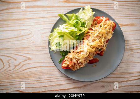Spitz rote Paprika gebacken mit Reis, Thunfisch und Käse, Salatsalat mit Petersilie auf einem grauen blauen Teller, rustikaler Holztisch, Kopierraum Stockfoto
