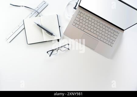 Silbergrauer Laptop mit leerem Bildschirm, Notebook, Stift und Brille auf weißem Schreibtisch, Kopierfläche, Blick von oben Stockfoto