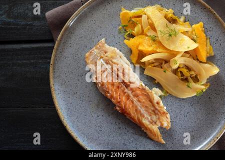 Kabeljaufisch mit Fenchelgemüse und orangefarbenen Scheiben auf einem blauen Teller und einem dunklen Tisch, hohe Ansicht von oben, ausgewählter Fokus Stockfoto