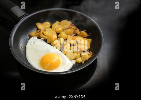 Spiegelei und Bratkartoffeln in einer schwarzen Pfanne auf dem Herd in der Küche, einfaches Kochen, Kopierraum, ausgewählter Fokus, schmale Schärfentiefe Stockfoto