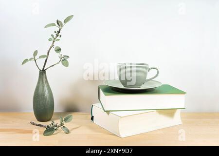 Holzschreibtisch oder -Tisch mit Büchern, grüner Teetasse und Salbeizweige in einer kleinen Keramikvase an einer grauen weißen Wand, Kopierbereich, ausgewählter Fokus, schmal Stockfoto