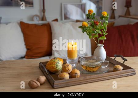 Tablett mit einer Tasse Tee, beleuchteter Kerze und Herbstdekoration auf einem Tisch im Wohnzimmer, gemütliches Zuhause in der kalten Jahreszeit, Kopierraum, ausgewählter Fokus Stockfoto