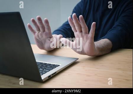 Hände in Verteidigungsgeste gegen einen Laptop, um weitere Arbeiten an einem gehackten System oder andere Gefahren und Beleidigungen, Online-Risiken im Geschäft zu vermeiden Stockfoto