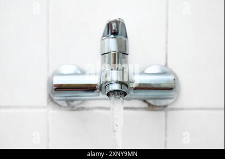 Badewannen- oder Wasserhahn mit fließendem Wasser an einer weißen gefliesten Wand in einem älteren Badezimmer, Kopierbereich, ausgewählter Fokus, sehr schmale Schärfentiefe Stockfoto