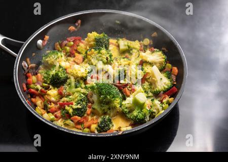 Vegetarisches Curry mit Brokkoli und anderem Gemüse in einer dampfenden Pfanne auf schwarzem Herd, asiatisches Kochkonzept, Kopierraum, ausgewählter Fokus Stockfoto