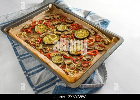 Backofen Gemüse mit Kräutern und Gewürzen auf einem Backblech auf einem blauen Küchentuch und einem weißen Tisch, mediterrane vegetarische Gerichte, Kopierraum Stockfoto