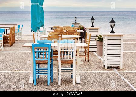 Holzstühle und Tische in Blau und Weiß in einer Taverne auf der Terrasse am Meer, Touristenziel in Chalkidiki, Griechenland, ausgewählter Fokus Stockfoto