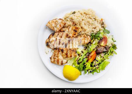 Gegrilltes Hähnchenfilet mit gemischtem Salat, Reis und Zitrone, mediterranes Gericht auf einem Teller, weißer Tisch, Kopierraum, Blick aus einem hohen Winkel von oben Stockfoto