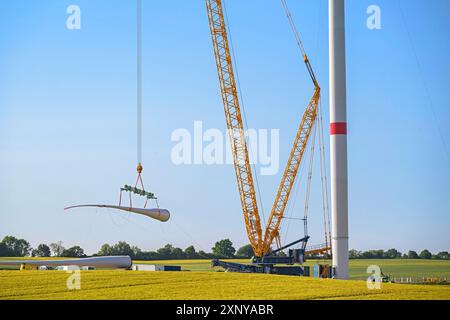 Ein Riesenkran hebt ein Windturbinenschaufel an, um es auf dem Turm zu installieren, Baustelle für Schwerindustrie, Konzept für Elektrizität, erneuerbare Energien Stockfoto